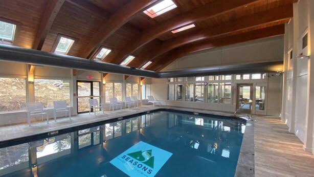 An indoor swimming pool with a wooden ceiling and skylights, surrounded by lounge chairs and a sign reading "SEASONS ON MONTLIT SNOW". - Seasons On Mount Snow - Ski-in/Ski-out  (Dover)