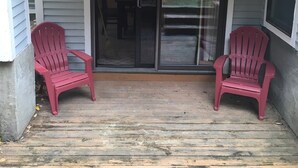 A covered porch with two red Adirondack chairs, a sliding glass door, and a concrete wall. - Seasons On Mount Snow - Ski-in/Ski-out  (Dover)