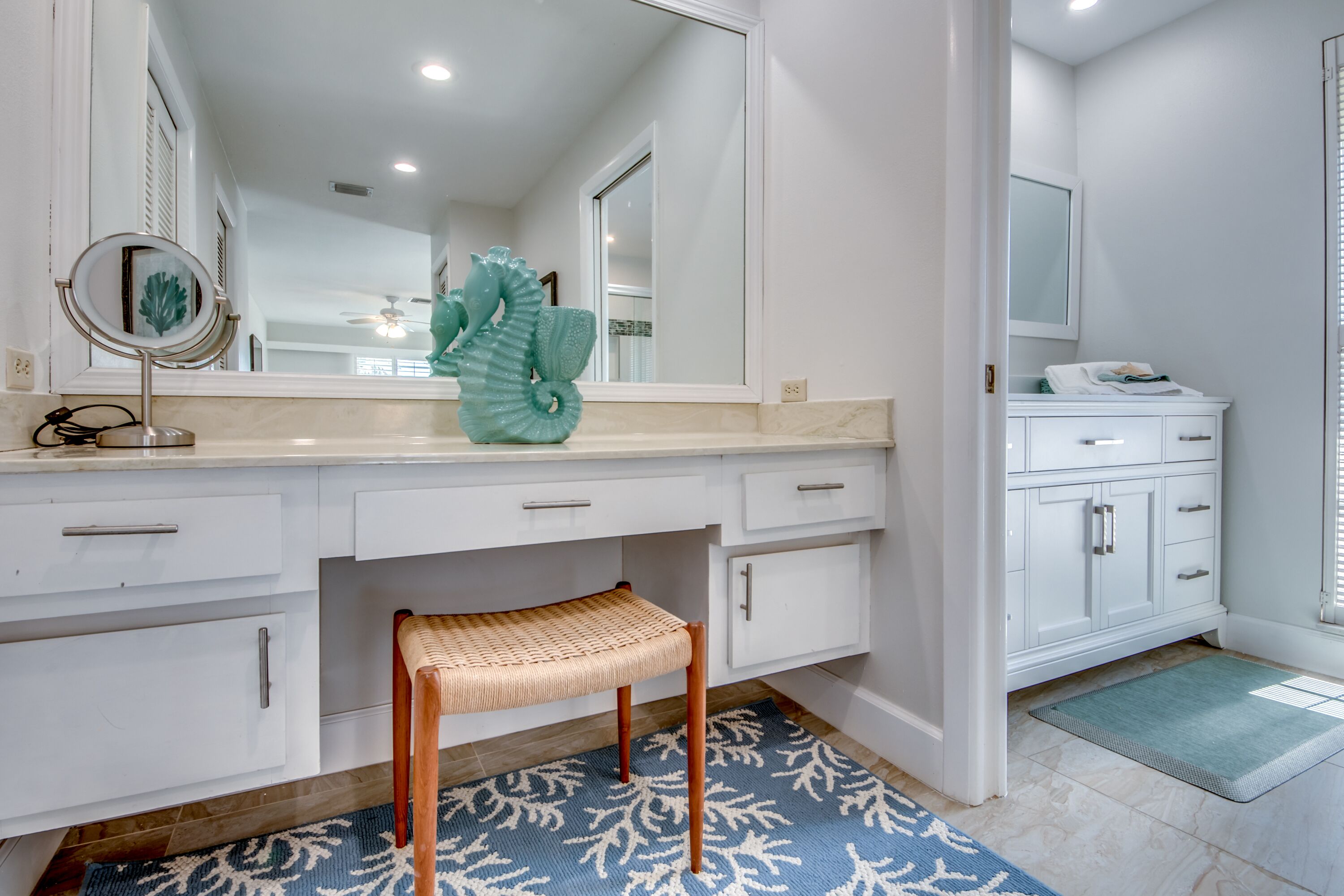 A bathroom with a vanity, a mirror, a seahorse decoration, a towel, and a wooden stool.
