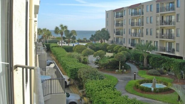 A multi-story building with balconies, a landscaped courtyard with a fountain, and a view of the sea. - Cozy beach unit setup for vacations with kids or Couples!  (St Simons Island)