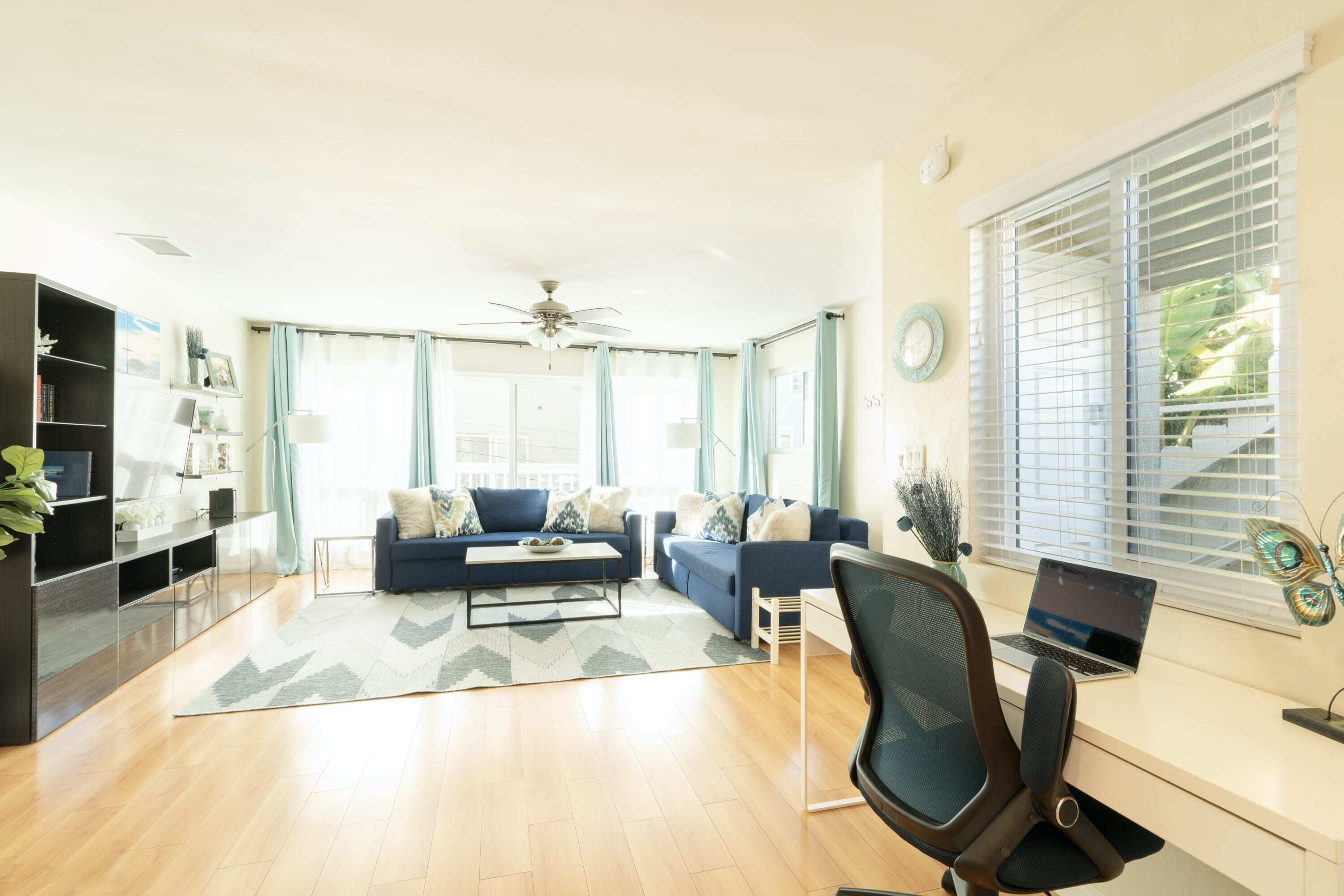 A modern living room with a blue sofa set, a coffee table, a TV, and a desk with a laptop.