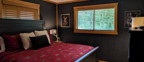 Une chambre à coucher avec un lit, une fenêtre avec des stores, une table de chevet et une lampe.