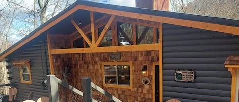 Una cabaña de troncos con fachada de madera, un porche con sillas Adirondack y una escalera que lleva a la entrada.