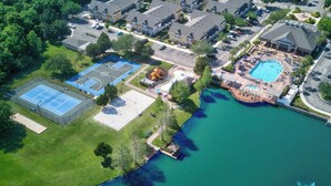 Vue aérienne d’un quartier résidentiel avec une piscine, des courts de tennis et une grande maison dotée d’une allée.