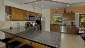 A modern kitchen with granite countertops, stainless steel appliances, wooden cabinets, and a large island with bar stools. - Vacation Townhome - Hot Tub, Red Rock Views, Walk to Dining/Trails (Sedona)