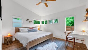 Un dormitorio con cama de madera, un escritorio y una silla. Hay ventanas con vistas a zonas verdes.