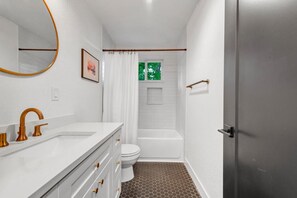 A bathroom with a white vanity, a toilet, a bathtub, and a shower curtain.