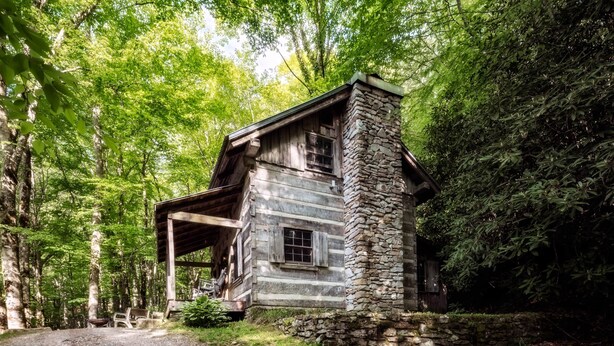 A rustic cabin with a stone chimney, wooden exterior, and a porch area. - Historic Creekside Cabin with Luxury Amenities, WiFi, Fireplace, Private Trails (Robbinsville)