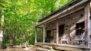 A rustic cabin with a porch, wooden furniture, and a stone pathway leading to the entrance. - Historic Creekside Cabin with Luxury Amenities, WiFi, Fireplace, Private Trails (Robbinsville)