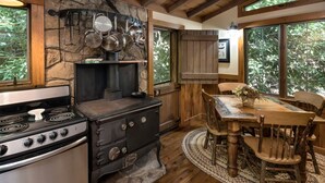 A rustic kitchen with a stone wall, wooden cabinets, and a large window. - Historic Creekside Cabin with Luxury Amenities, WiFi, Fireplace, Private Trails (Robbinsville)