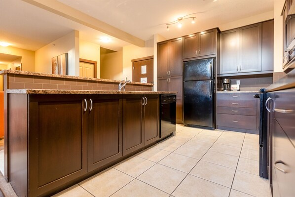 A modern kitchen with dark wood cabinets, a granite countertop, and stainless steel appliances. - Top Floor with AC. Hot Tub. Mtn. Views (Fernie)