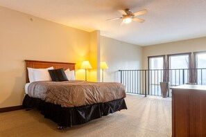 A hotel room with a bed, two bedside lamps, a ceiling fan, a balcony with a railing, and large windows. - Top Floor with AC. Hot Tub. Mtn. Views (Fernie)
