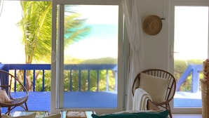 A room with a view of the ocean, a blue balcony, wicker chairs, and a woven basket.