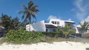 A modern beachfront property with a white building, palm trees, and a sandy beach.