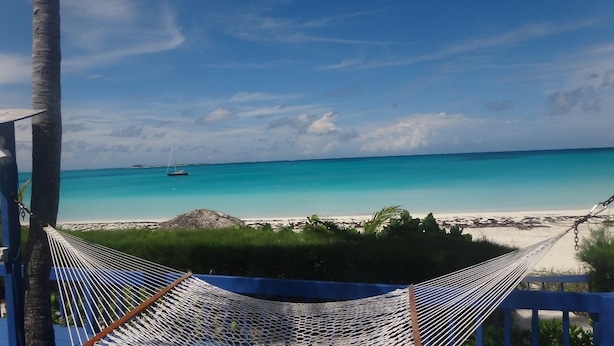 A hammock overlooking a beach with clear turquoise water and a distant sailboat.