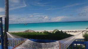 Un hamac suspendu au-dessus d’une plage, avec une vue sur une eau turquoise et limpide et un voilier à l’horizon.
