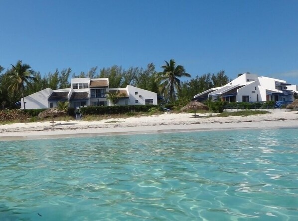 Une propriété située en bord de mer, dotée d’une architecture moderne, d’une plage de sable et d’une eau turquoise cristalline.