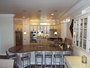 A kitchen with a central island, bar stools, stainless steel appliances, and pendant lighting.