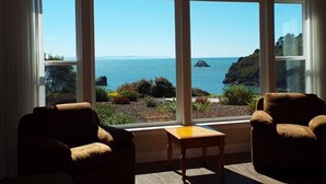 A room with large windows offering a view of the sea and a rocky coastline. There are two chairs and a small table. - Incredible Ocean Views 3 Bedrooms 3 Bathrooms (Trinidad)
