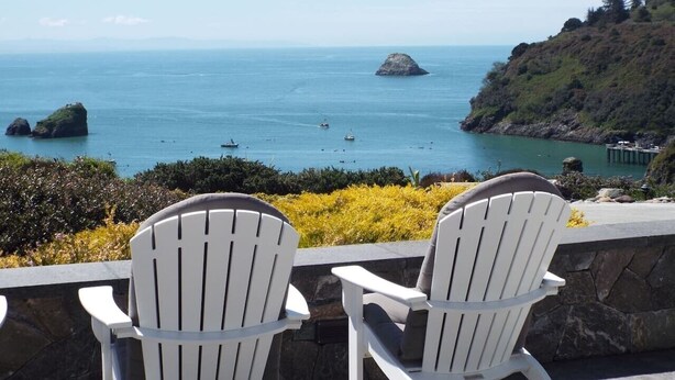 Two white chairs facing a coastal view with boats, rocky outcrops, and a pier. - Incredible Ocean Views 3 Bedrooms 3 Bathrooms (Trinidad)