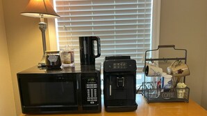 A kitchen counter with a microwave, coffee maker, and a coffee station with cups and a mug.