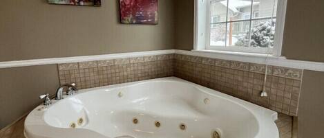 A bathroom with a freestanding bathtub, two wall-mounted artworks, and a window with blinds.