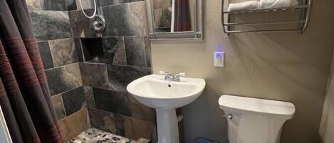 A bathroom with a shower, a sink, and a toilet. There is a towel rack with towels, a mirror, and a window.