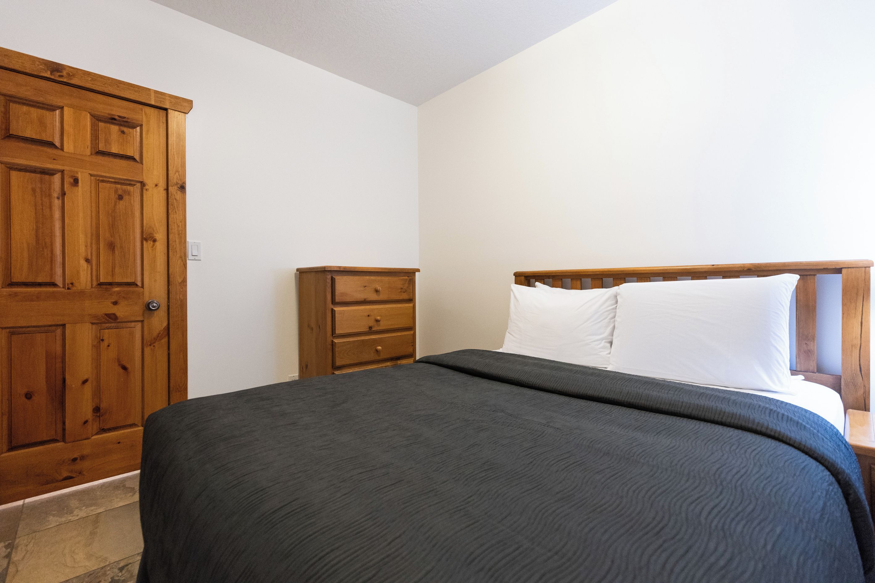 A bedroom with a bed, a wooden wardrobe, and a nightstand.