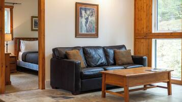 Une pièce avec un canapé en cuir noir, une table basse en bois et un tableau encadré accroché au mur.