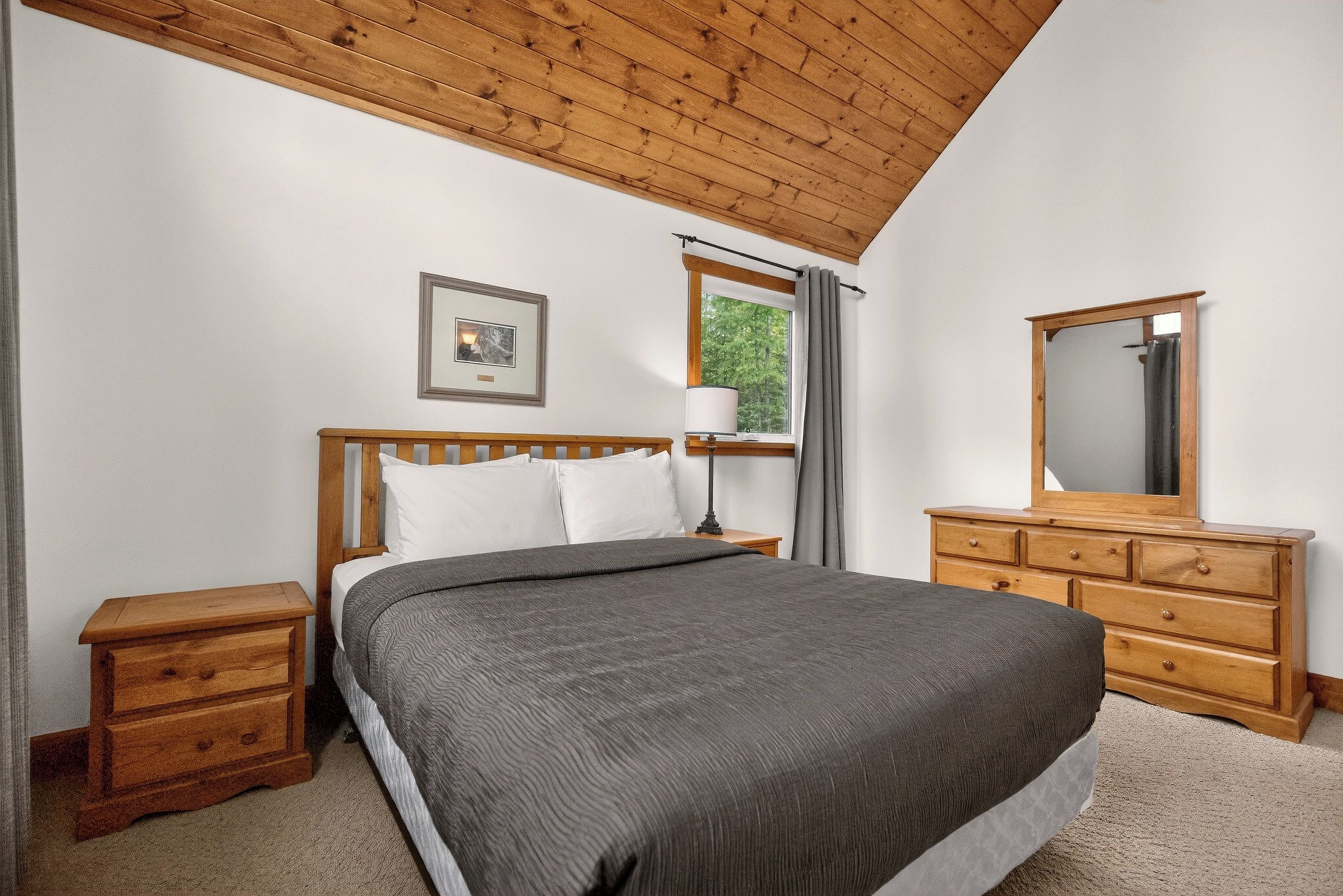 Une chambre à coucher avec un lit en bois, une table de chevet, une commode, un miroir et une fenêtre avec des rideaux.