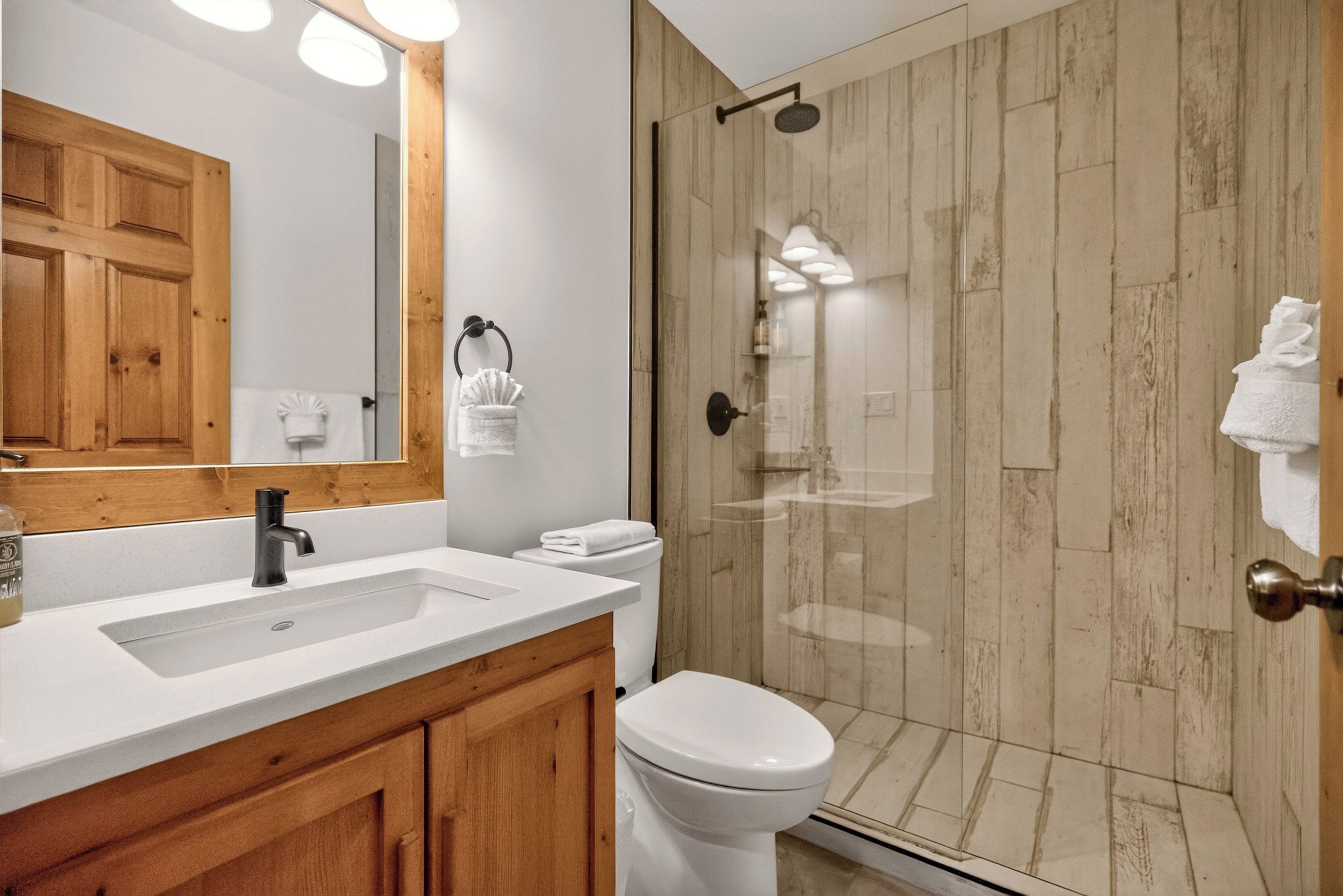 A modern bathroom with a wooden vanity, a large mirror, a toilet, and a glass-enclosed shower area.
