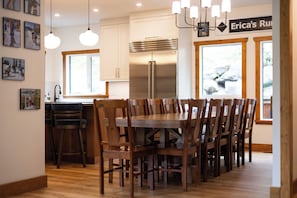 Une cuisine moderne avec un coin repas, des chaises en bois, un réfrigérateur en acier inoxydable et des luminaires suspendus.