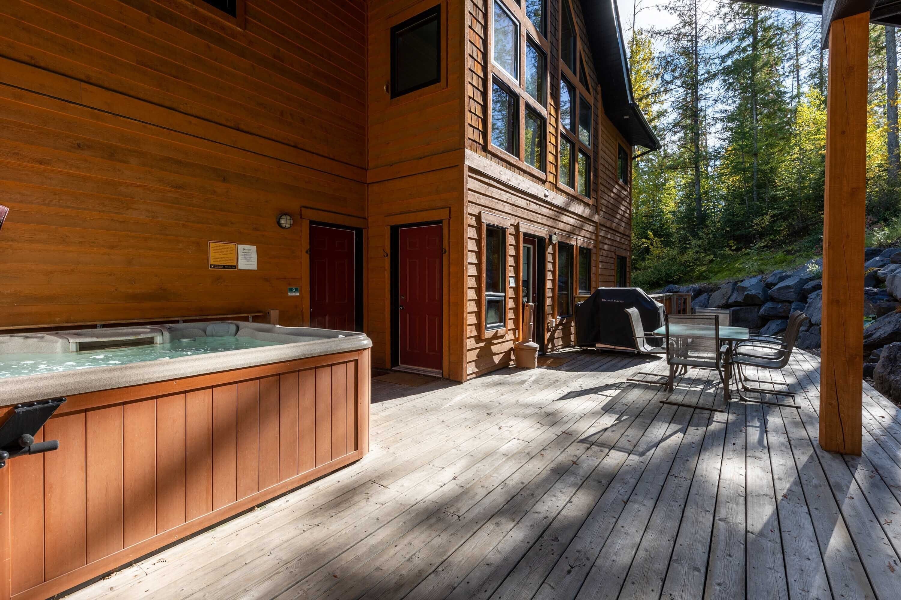 A wooden deck with a hot tub, outdoor seating, and a view of the forest.