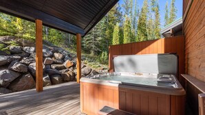 Une terrasse en bois avec un jacuzzi, des bancs en bois et un mur en pierre en arrière-plan.