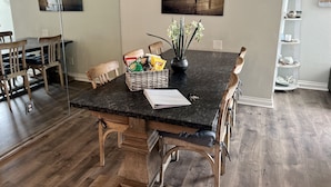 Et spiseområde med et mørkt granitbord, træstole, en kurv med snacks og en vase med blomster.