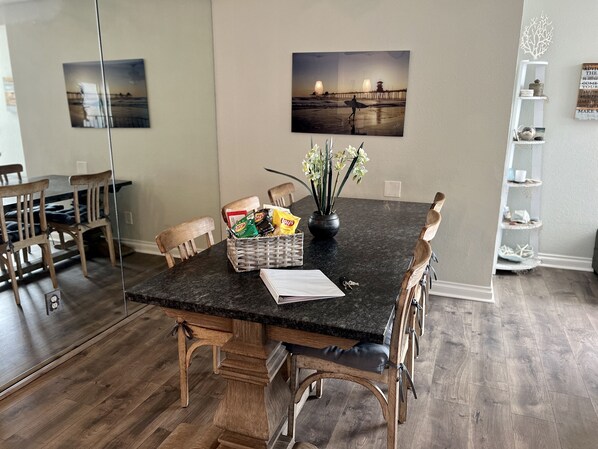 A dining area with a dark granite table, wooden chairs, a basket of snacks, and a vase of flowers.