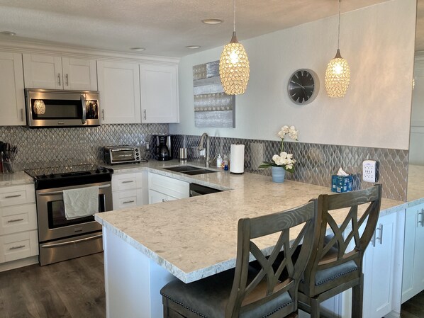 A modern kitchen with white cabinetry, stainless steel appliances, a marble countertop, and pendant lighting.