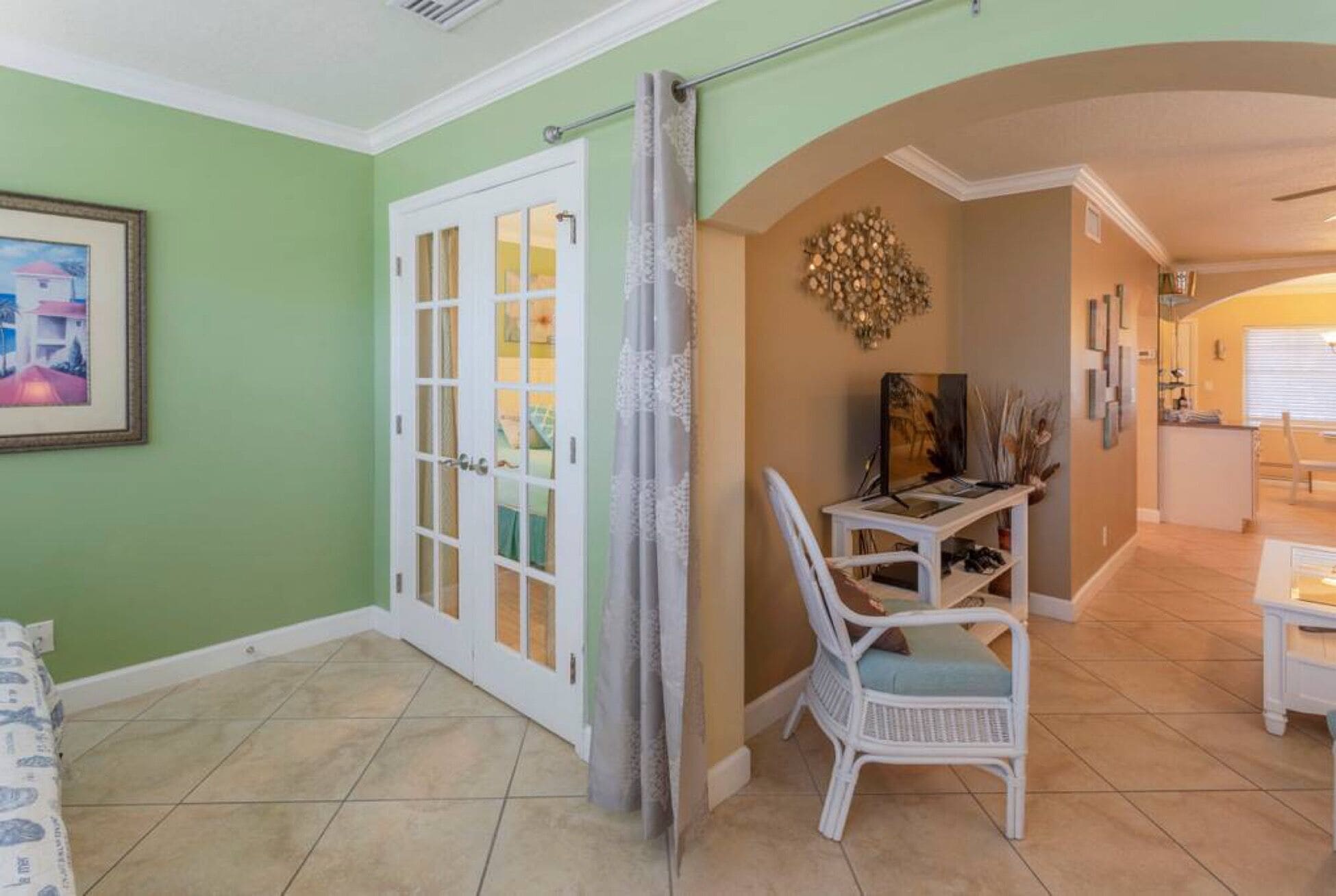 Une pièce avec un mur vert, une porte blanche dotée de panneaux de verre, une chaise en osier blanche, une petite table et un élément décoratif mural.