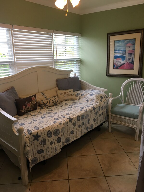 Un dormitorio con cama, una silla, una ventana con persianas y un cuadro enmarcado en la pared.