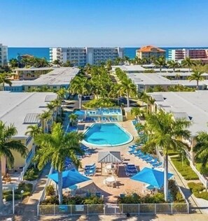 Un resort con piscina central rodeada de palmeras y sillas de descanso.