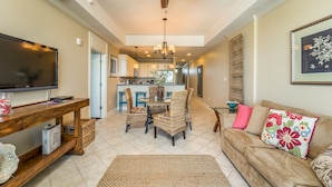 A spacious living room with a ceiling fan, a TV, a wooden coffee table, wicker chairs, and a sofa with floral cushions.