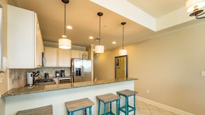 A kitchen with a central island, bar stools, and pendant lighting.