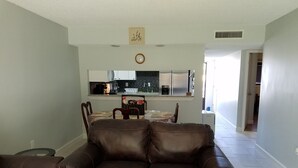 A living room with a brown leather sofa, a dining area with a table and chairs, and a kitchen in the background.