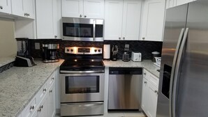 A modern kitchen with stainless steel appliances, white cabinetry, and a granite countertop.