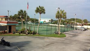 A tennis court with a fence, palm trees, and an American flag.