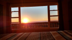 Una stanza con un letto e una grande finestra vista tramonto sull'oceano.