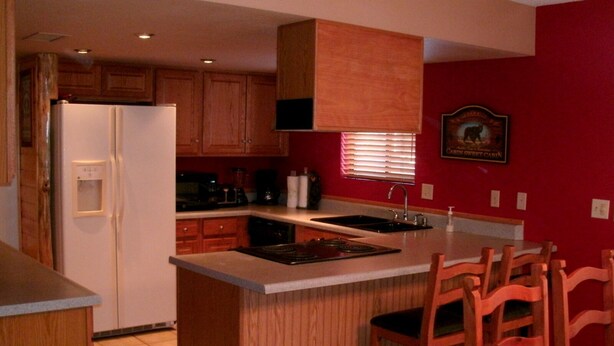 A kitchen with wooden cabinets, a refrigerator, a stove, a sink, and a dining area with chairs.
