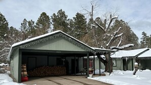 A covered garage with a snow-covered roof and a stack of firewood outside.