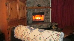 A cozy living room with a stone fireplace, wooden furniture, and a red curtain.