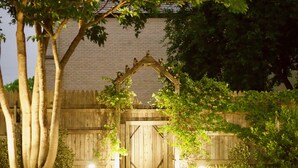 A wooden gate with a decorative arch, surrounded by lush greenery and a brick wall.